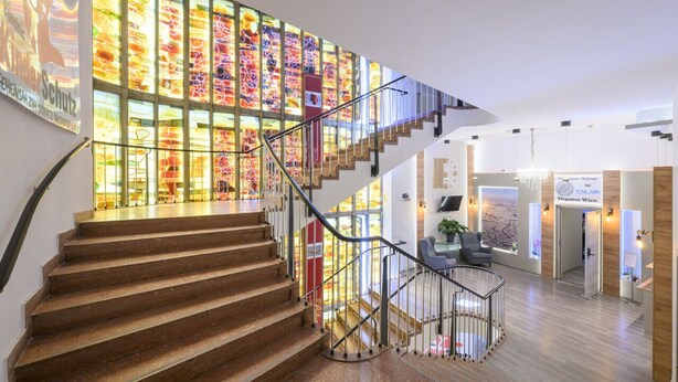 A modern hotel interior with a wooden staircase, a stained glass wall, and a reception area.