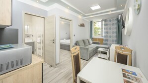 A compact hotel room with a kitchenette, a sofa, a small table, and a bed.