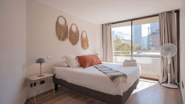 Una camera d'albergo con un letto, un comodino, una lampada e vista sugli edifici.