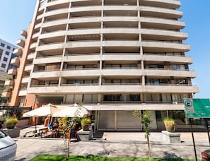 A multi-story building with balconies, a ground-level cafe, and a green sign indicating a nearby location.