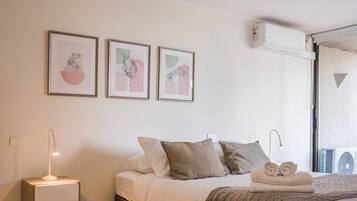 A bedroom with a bed, bedside tables, a wall-mounted air conditioner, and framed artwork on the wall.