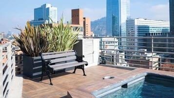 A rooftop pool with a bench, potted plants, and a cityscape view.