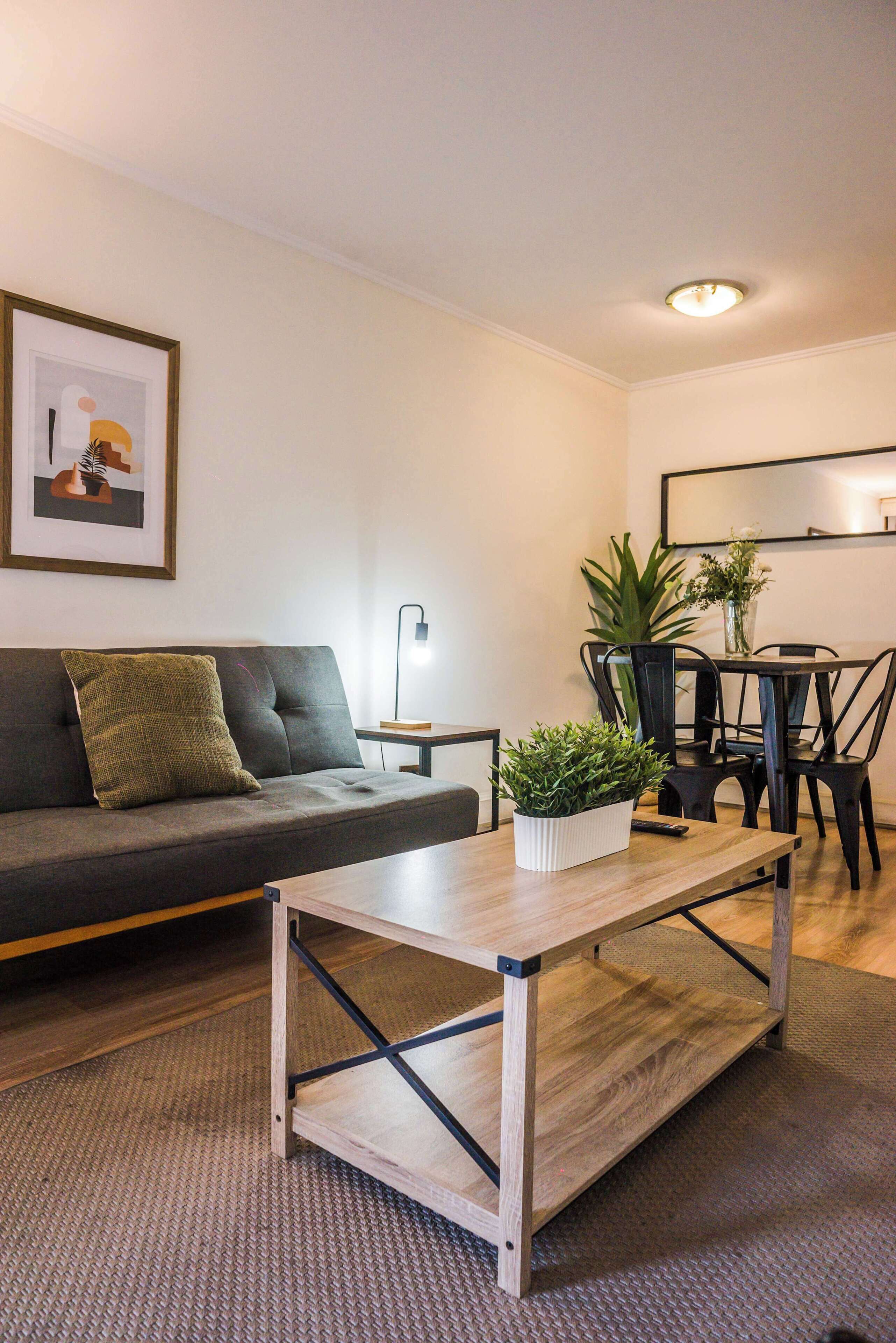 A modern living room with a sofa, a coffee table, a dining table with chairs, a floor lamp, and a potted plant.