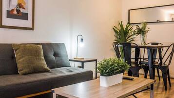 A modern living room with a sofa, a coffee table, a dining table with chairs, a floor lamp, and a potted plant.