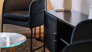 A room with a desk, a chair, a glass table, a vase with flowers, and a window with blinds. - Comfortable 1BR/1BA in Las Condes | Prime Location (Las Condes)