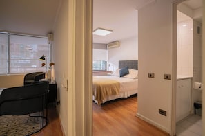 Ein Hotelzimmer mit Bett, Nachttisch, Lampe, Stuhl und Blick auf die Stadt durch das Fenster.