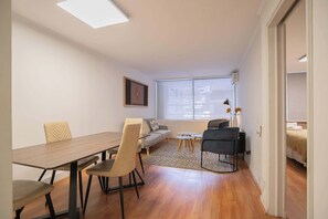 A modern living room with a wooden dining table, two sofas, a coffee table, and a view of the city through large windows.