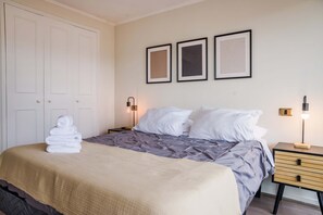 A hotel room with a bed, a nightstand, a lamp, and a door. - Chic 1BR Oasis in Las Condes: Pool and City Views (Las Condes)