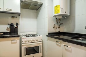 A kitchen with white cabinets, a gas stove, a built-in oven, a stainless steel sink, and a yellow caution sign. - Chic 1BR Oasis in Las Condes: Pool and City Views (Las Condes)