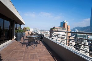 A balcony with outdoor seating, a large potted plant, and a view of city buildings.