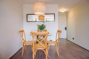 A dining area with a round table, four wooden chairs, a hanging light fixture, and a mirror on the wall.