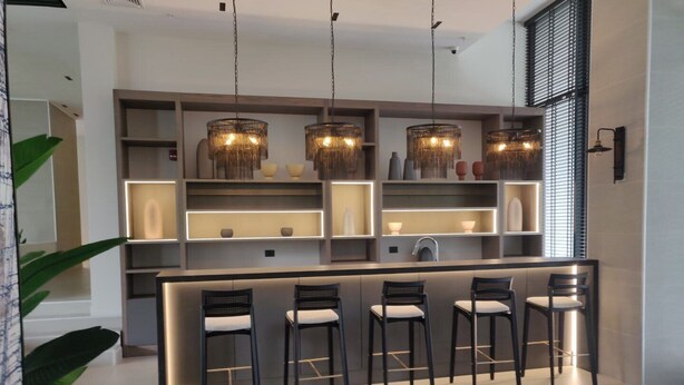 Una cocina moderna con una isla central, taburetes de bar, iluminación colgante y estanterías empotradas.