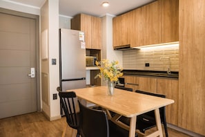 A compact kitchen with wooden cabinets, a built-in microwave, and a dining area with a table and chairs. - Family Adventure Charming 2BR In Providencia For 5 (Providencia)