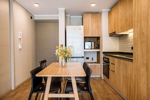 A modern kitchen with wooden cabinets, a built-in oven, and a dining area with a wooden table and chairs. - Family Adventure Charming 2BR In Providencia For 5 (Providencia)