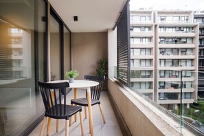 Private balcony with a round dining table, seating for outdoor meals, and leafy potted plants overlooking the modern courtyard. - Family Adventure Charming 2BR In Providencia For 5 (Providencia)