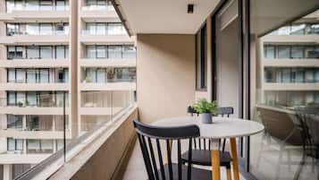 Un balcón con una mesa redonda y sillas, una planta en maceta y vistas de un edificio de varios pisos.