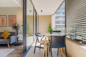 Un balcón con mesa y sillas, un sofá, un ventilador y una ventana con persianas.