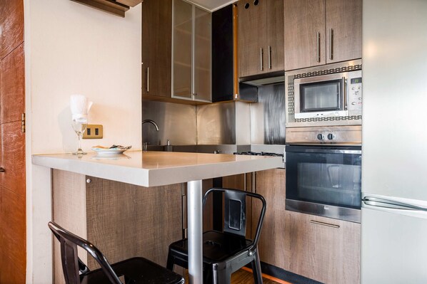 A compact kitchen with a built-in microwave, oven, and a small dining area with a chair and table.