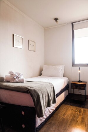 Une chambre à coucher avec un lit, des oreillers, une table de chevet avec une lampe, et deux tableaux encadrés accrochés au mur.