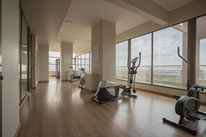 Une salle de sport équipée de machines de cardio, dotée de grandes fenêtres et offrant une vue sur la ville.