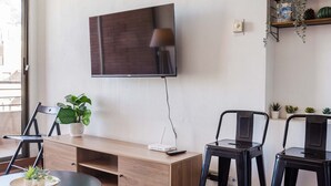 Ein modernes Wohnzimmer mit Flachbildfernseher, einer Holz-Unterhaltungsecke, zwei schwarzen Sesseln, einem runden Couchtisch und einem Blumentopf.