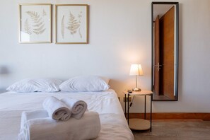 A neatly made bed with white linens, a rolled towel, and two framed botanical prints on the wall. - Chic 2BR | Your Cozy Getaway Oasis in Las Condes (Las Condes)