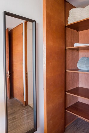Un couloir avec une porte en bois, un miroir et une étagère en bois sur laquelle sont posés une serviette pliée et une couverture.