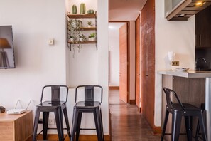 Une cuisine moderne équipée d’un four encastré, d’un évier et d’un plan de travail. On y trouve deux chaises noires et une petite table sur laquelle sont posés un ordinateur portable et un objet décoratif.