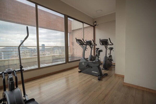 Une salle de sport équipée de machines de cardio et dotée d’une grande fenêtre donnant sur le paysage urbain.