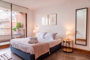 Une chambre d’hôtel avec un lit, des lampes de chevet, une grande fenêtre et un balcon agrémenté d’une plante.