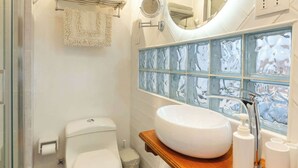 Ein Badezimmer mit Toilette, Waschbecken, Spiegel und einer Rückwand aus Glasfliesen.