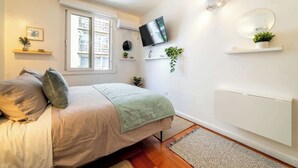 Ein Schlafzimmer mit Bett, Fernseher, Fenster, Heizkörper und einer Pflanze.