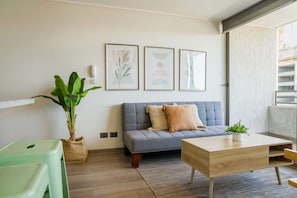 A modern living room with a grey sofa, a wooden coffee table, a green plant, and framed artwork on the wall. - Modern 1BR Retreat in Nunoa | Ultimate Comfort (Ñuñoa)