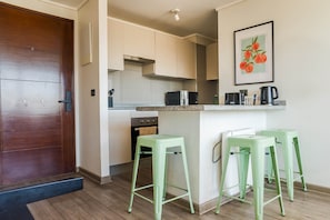 A modern kitchen with a wooden door, white cabinets, a microwave, and two green bar stools. - Live the authentic atmosphere of Barrio Italia (Ñuñoa)
