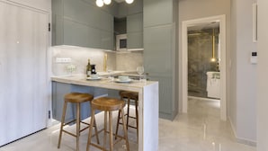 A modern kitchen with a central island, bar stools, and a built-in microwave. - Gold Apartment (Nea Smirni)