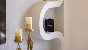 A modern interior with a white, wavy wall design, a flat-screen TV, and two decorative candle holders. - Gold Apartment (Nea Smirni)