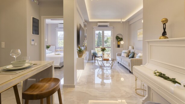 A modern living room with a sofa, coffee table, and a dining area with a table and chairs. - Gold Apartment (Nea Smirni)