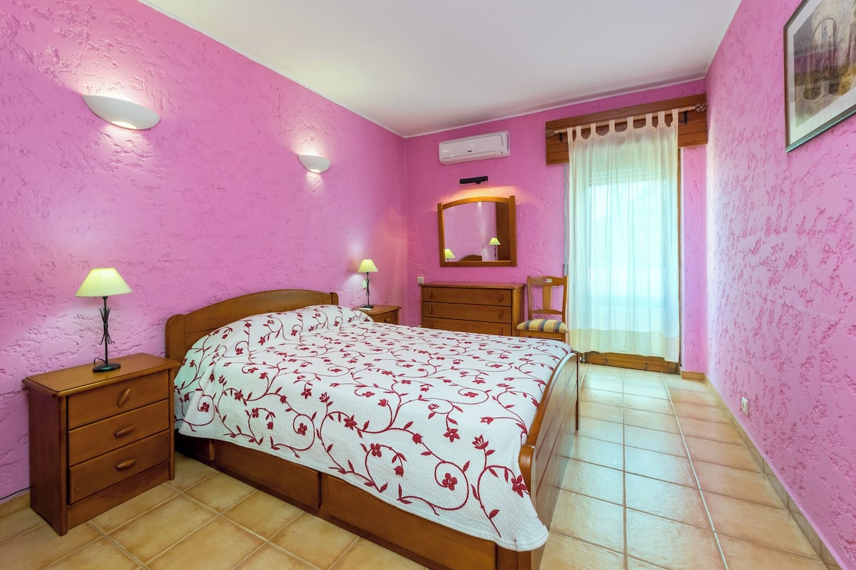 A bedroom with a bed, nightstands, a dresser, a mirror, and a window with curtains.