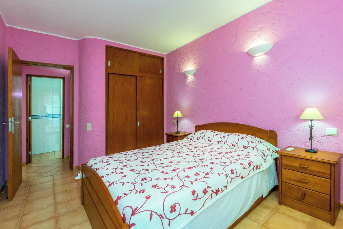 A bedroom with a bed, bedside tables, a wardrobe, and a door leading to another room.