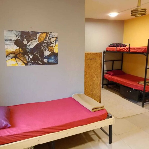 A dormitory room with bunk beds, a single bed, a wooden partition, and a painting on the wall.