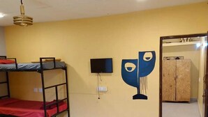 Une pièce avec des lits superposés, un téléviseur, une œuvre d’art murale, une armoire en bois et un tapis tissé sur le sol.