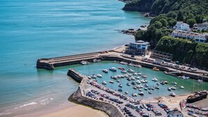 A coastal marina with boats, a parking area, and buildings on a cliff. - Rainbow Leap - 5 Bed Holiday Home - Saundersfoot (Saundersfoot)