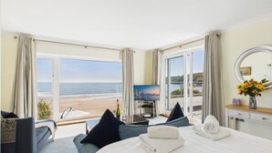 A hotel room with a large bed, a TV, a desk, and a view of the beach. - Rainbow Leap - 5 Bed Holiday Home - Saundersfoot (Saundersfoot)