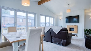 Een moderne woonkamer met een bank, een televisie en een open haard. Er zijn grote ramen en een balkon te zien.