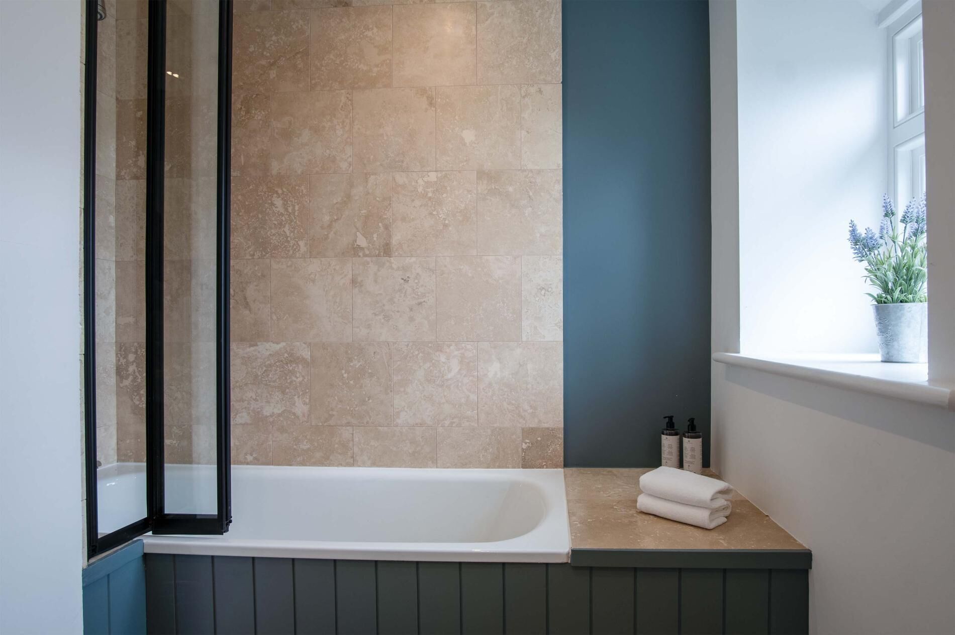 Une salle de bain avec une baignoire, une fenêtre avec une plante et une serviette posée sur le comptoir.