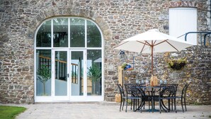 Ein Steinhaus mit einem großen Bogenfenster und einer Terrasse mit Tisch und Stühlen.