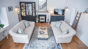 Ein Wohnzimmer mit zwei beigefarbenen Sofas, einem Couchtisch, einem gemusterten Teppich, einem Fernseher und einem Kamin.