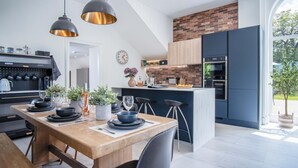 Eine moderne Küche mit Backstein-Spritzschutz, einem Essbereich mit Holztisch und einem großen Fenster mit Blick auf einen Garten.