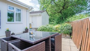 A patio with a glass-top table and wicker chairs, a white building with windows, and a wooden fence. - Clover Cottage - 2 Bedroom Cottage - Begelly (Kilgetty)