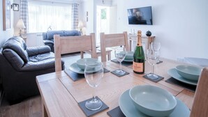 A dining area with a wooden table set for two, two wine glasses, a bottle of wine, and matching bowls and plates. - Clover Cottage - 2 Bedroom Cottage - Begelly (Kilgetty)